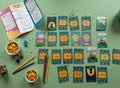 All 22 Qur'anic Arabic learning cards spread out with instruction booklet, snacks, colored pencils and toys on sage green background